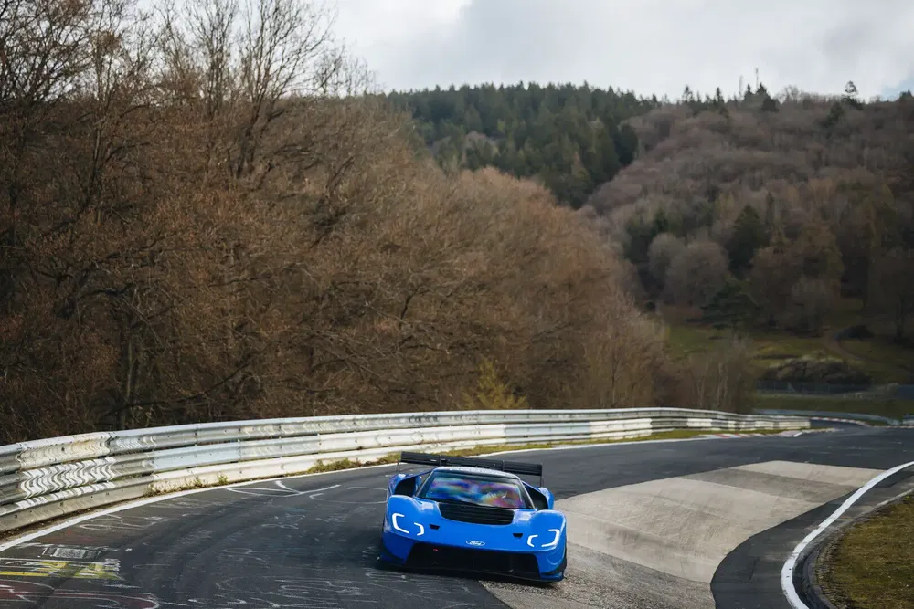 Voiture de sport Ford GT bleue sur circuit Nürburgring entouré de forêt automnale.