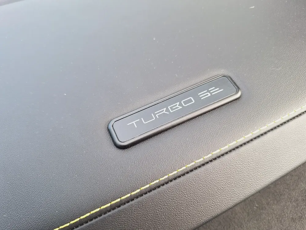 Dashboard Taycan Turbo S met zwart lederen badge en gele stiksels.