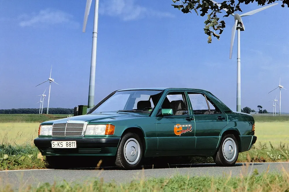 Mercedes-Benz vintage vert devant des éoliennes dans un paysage champêtre.