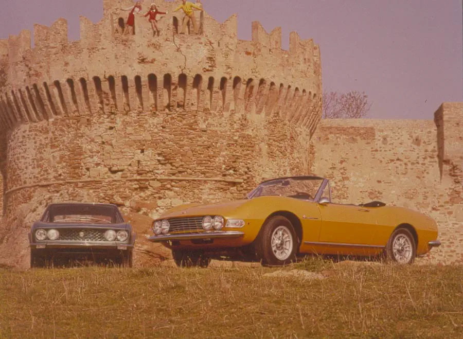 Voiture décapotable Fiat devant un château médiéval, avec une berline en arrière-plan.