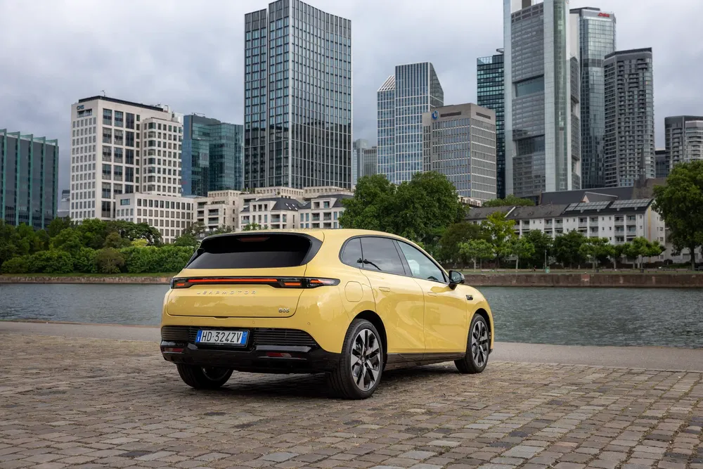 MG4 électrique jaune au bord de l'eau, fond de gratte-ciels urbains.
