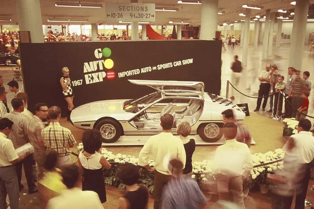 Auto-expo 1967 met futuristische sportwagen met open vleugeldeuren, omringd door bezoekers.
