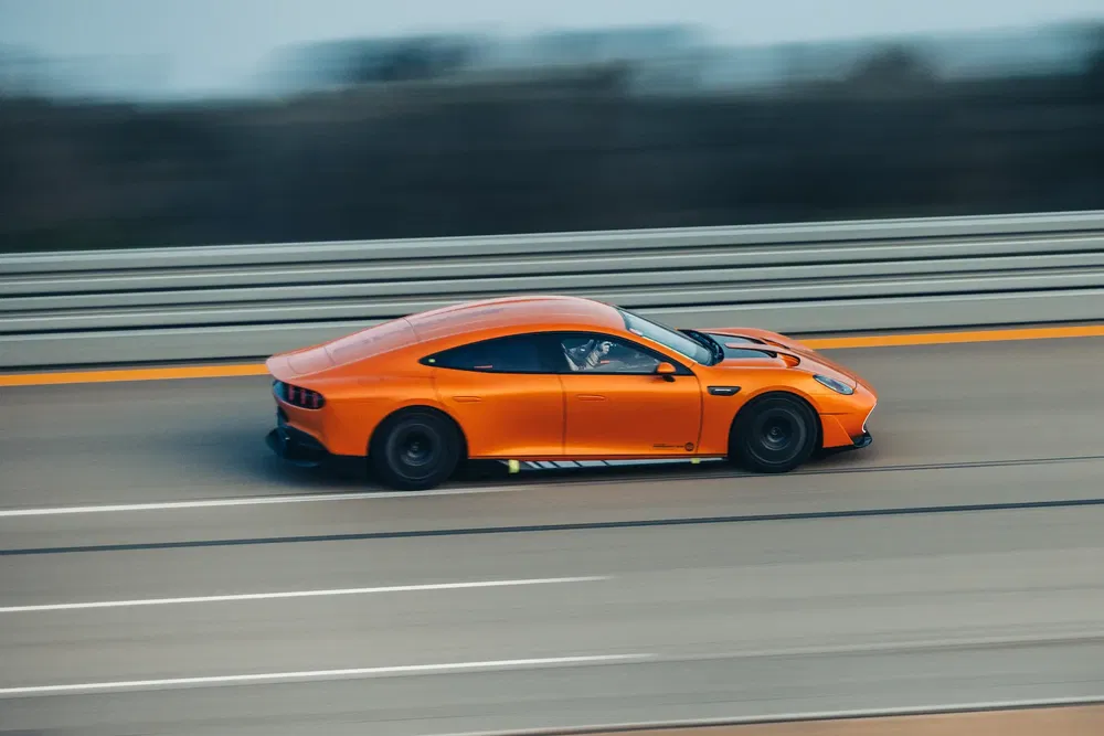 Voiture sport orange en mouvement rapide sur une autoroute, fond flou.