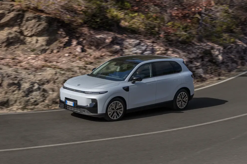 Moderne witte SUV rijdt op kronkelige bergweg met rotsachtige achtergrond.