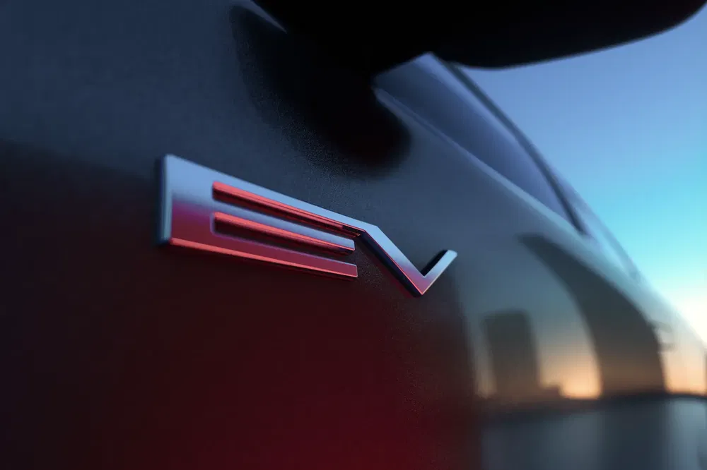 EV-logo op de carrosserie van een elektrische auto bij zonsondergang.