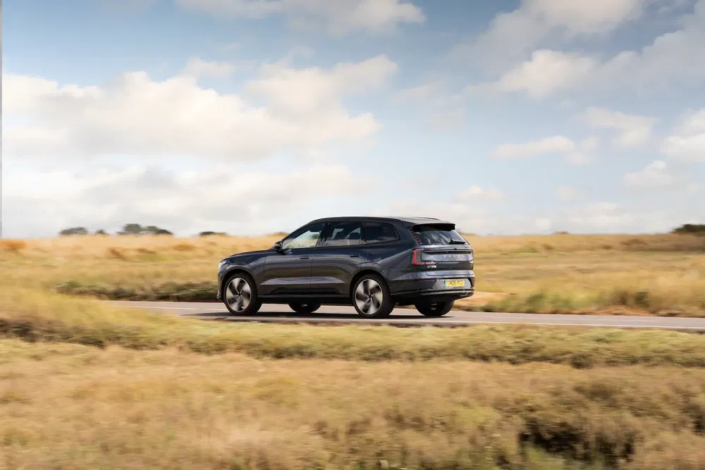 SUV Volvo roulant sur route champêtre sous ciel bleu, atmosphère automnale.