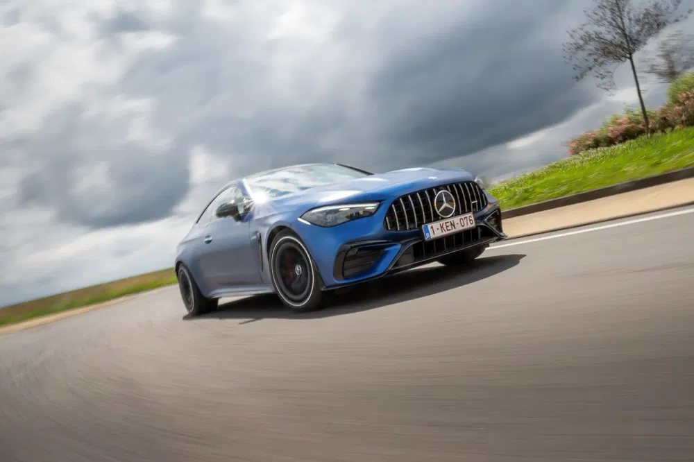 Mercedes AMG GT bleue roulant sur route sinueuse sous ciel nuageux.
