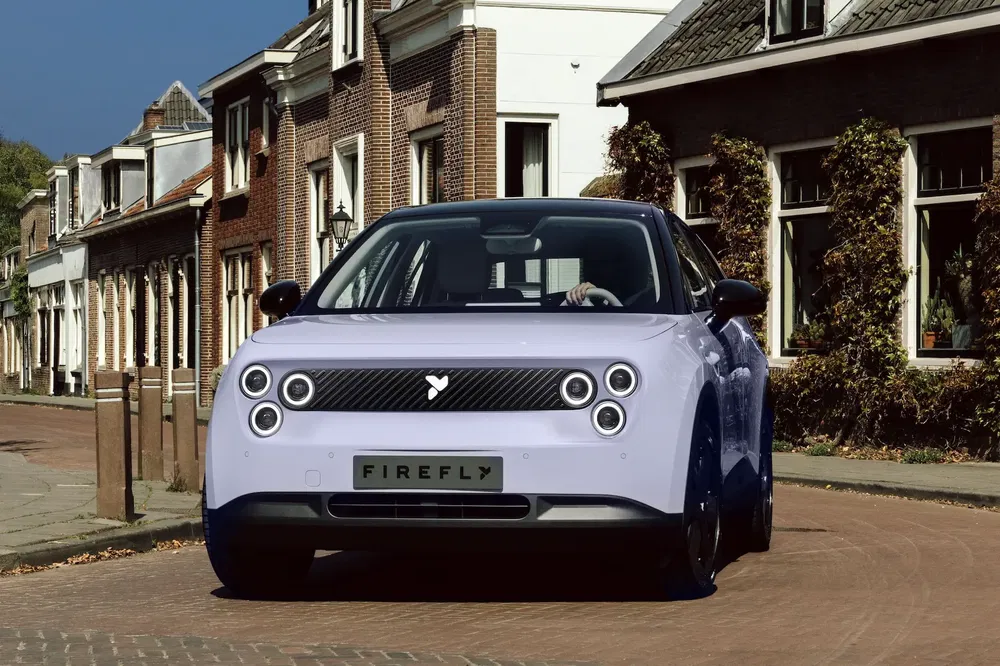 Voiture électrique Firefly dans une rue pavée, style rétro avec phares circulaires distinctifs.