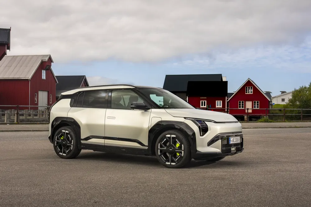 Kia EV9 stationné devant des bâtiments rouges et noirs sous un ciel nuageux.