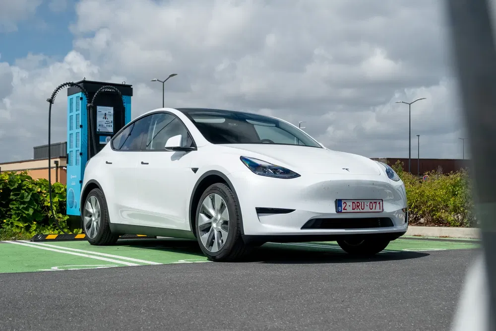 Tesla Model Y blanche en charge à une borne publique sous un ciel nuageux.