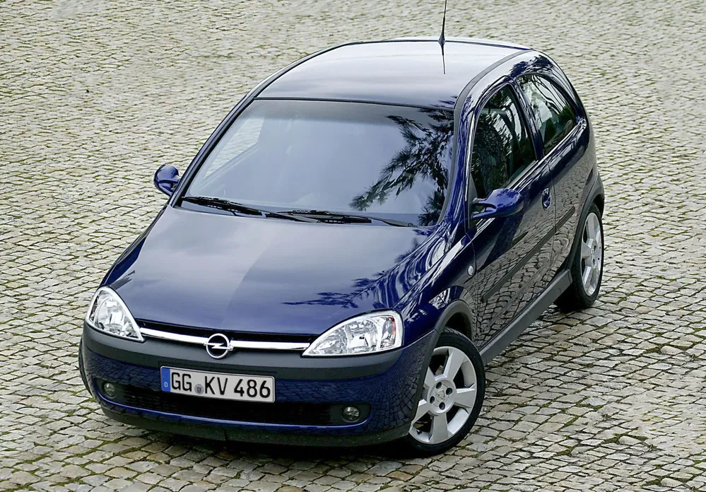 Opel Corsa bleu foncé garée sur route pavée, vue de dessus.