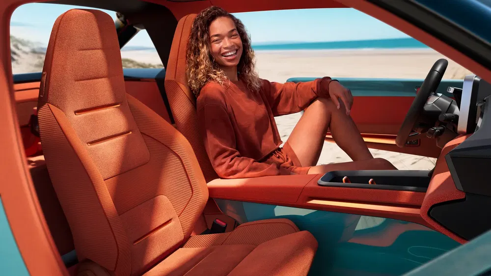 Moderne auto-interieur met oranje stoelen, lachende vrouw op achtergrond aan het strand.