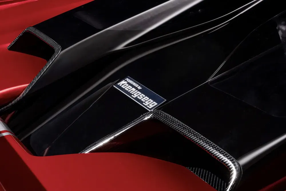 Détail du capot d'une supercar rouge avec le logo Koenigsegg, design aérodynamique.