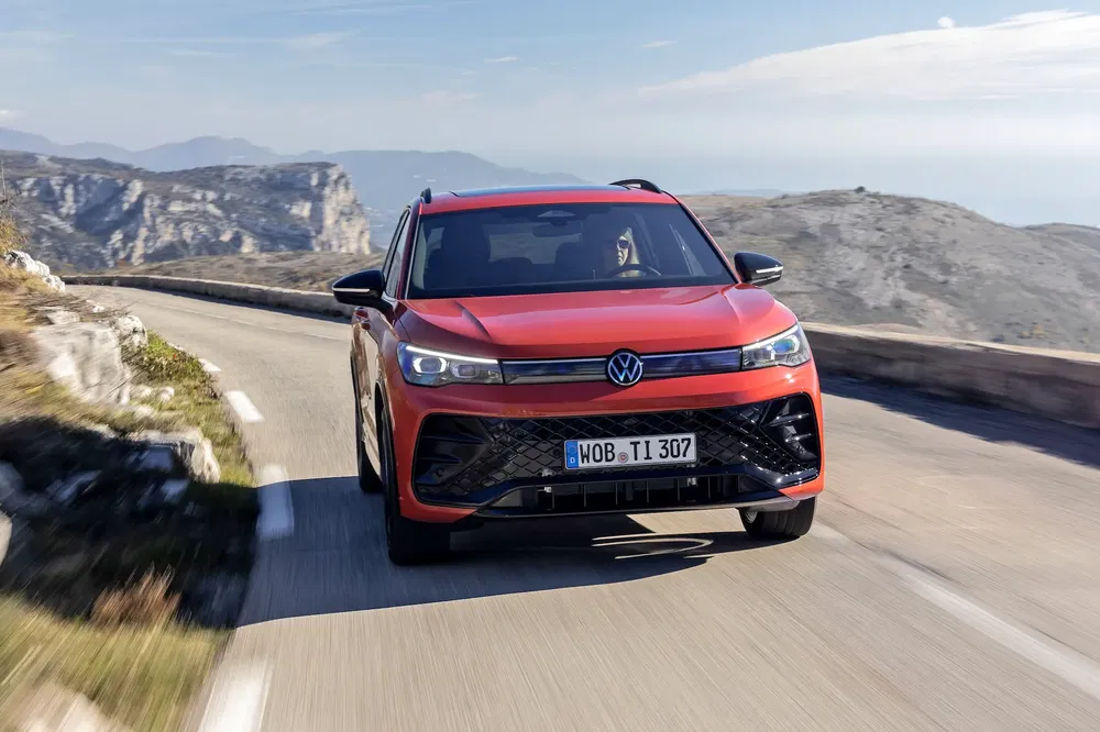 Volkswagen T-Roc rouge roulant sur une route de montagne sinueuse sous un ciel clair.