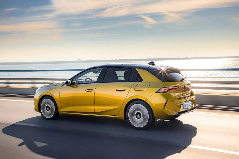 Gele Opel Astra die over een zonnige brug langs de zee rijdt.