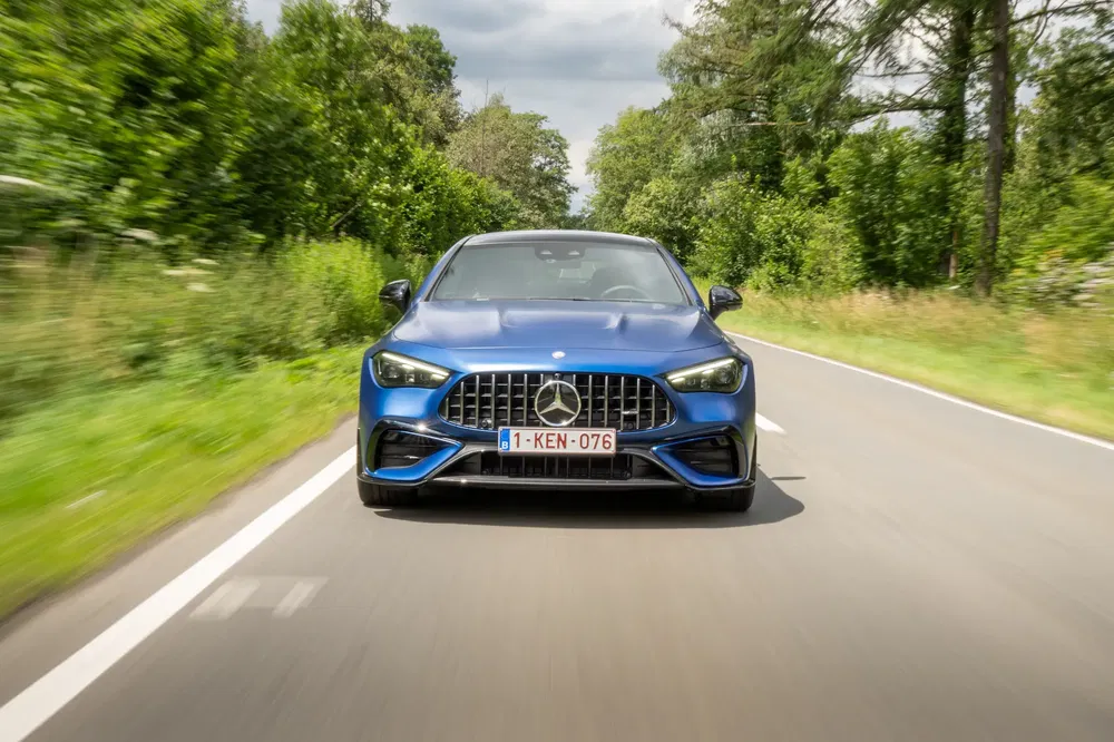 Mercedes-Benz bleu roulant sur une route bordée d'arbres, plaque belge visible.