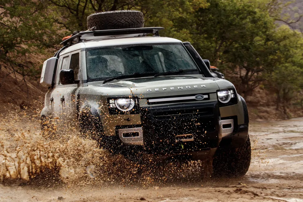 Land Rover Defender rijdt door modder op een offroad pad in de natuur.