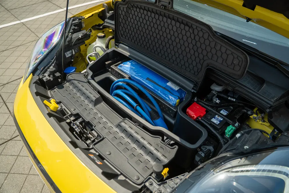 Voorkoffer van gele elektrische Renault 5 met laadkabels en geïntegreerde opslag.