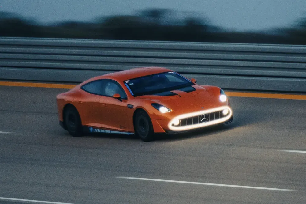 Voiture de sport Mercedes orange sur circuit de course, phares allumés la nuit.