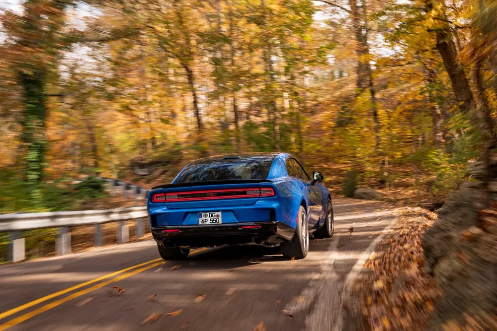 Dodge Charger bleu conduisant sur une route sinueuse entourée de feuillage d'automne.