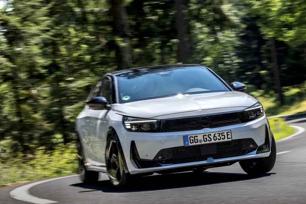 Opel Astra blanche prenant un virage sur une route boisée.