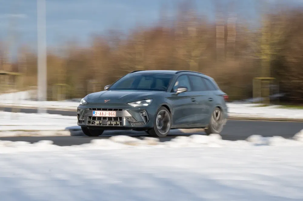 Grijze Cupra Leon rijdt op besneeuwde weg met wazige achtergrond.
