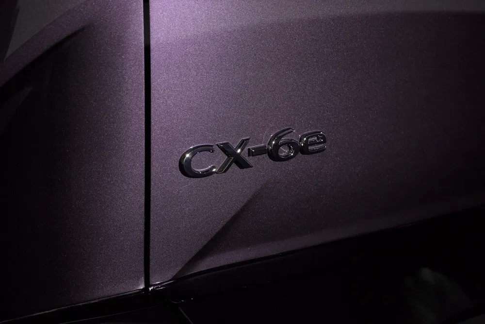 Logo Mazda CX-6e sur carrosserie violette, mettant en avant le modèle hybride.