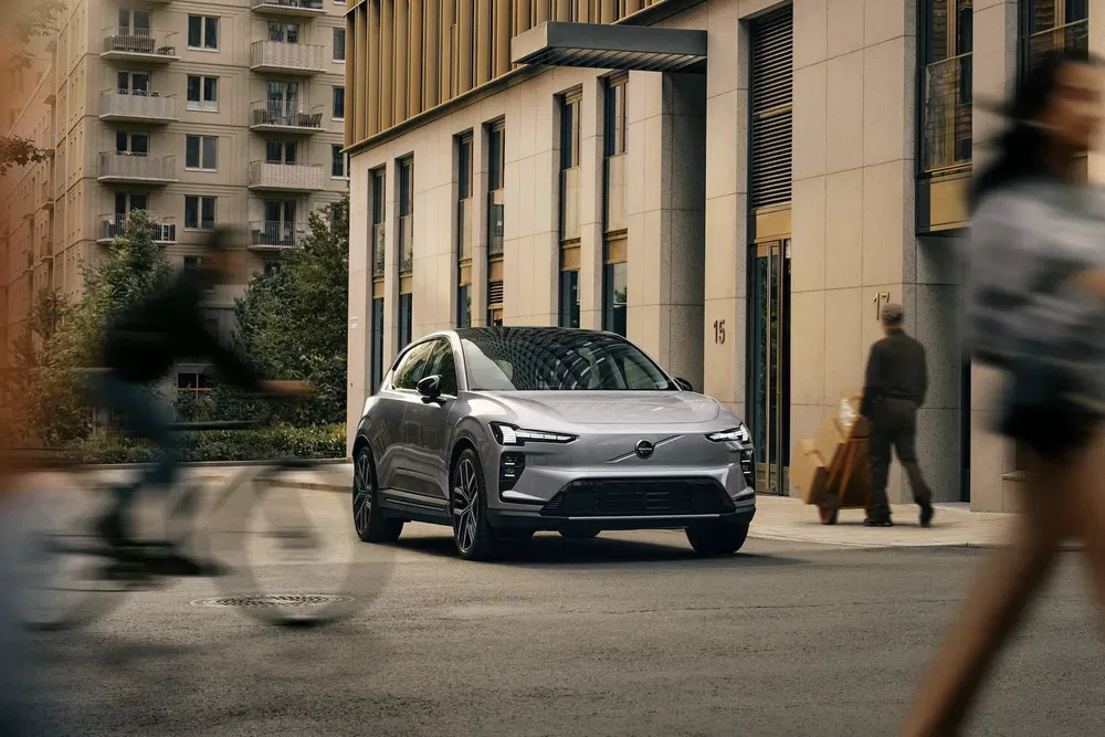Volvo EX30 grise stationnée dans une rue urbaine animée, cyclistes et piétons en mouvement.