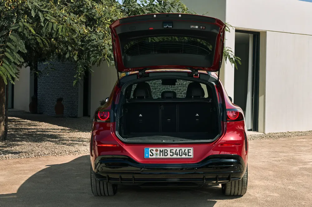 Mercedes-Benz EQB rouge avec coffre ouvert, résidence moderne en arrière-plan.