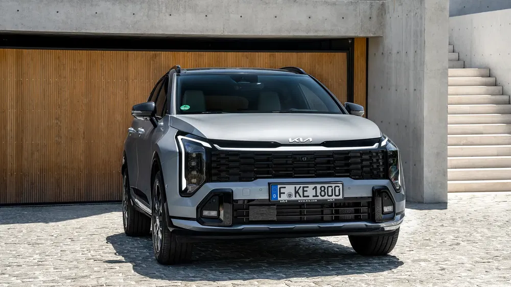 SUV Kia Sportage gris, stationné devant un garage moderne en béton et bois.