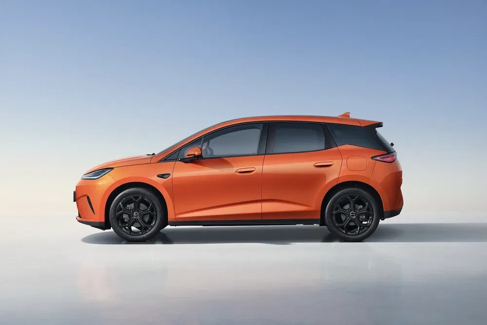 BYD Dolphin orange stationné sous un ciel bleu pur, design moderne et aérodynamique.