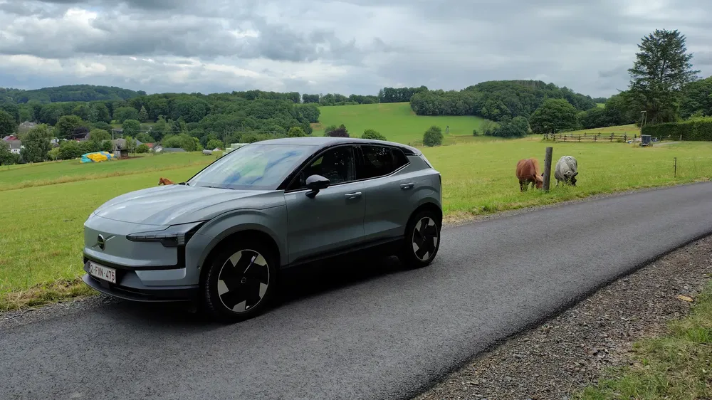Volvo EX30 sur route de campagne, pâturages verts et vaches à l'arrière-plan.