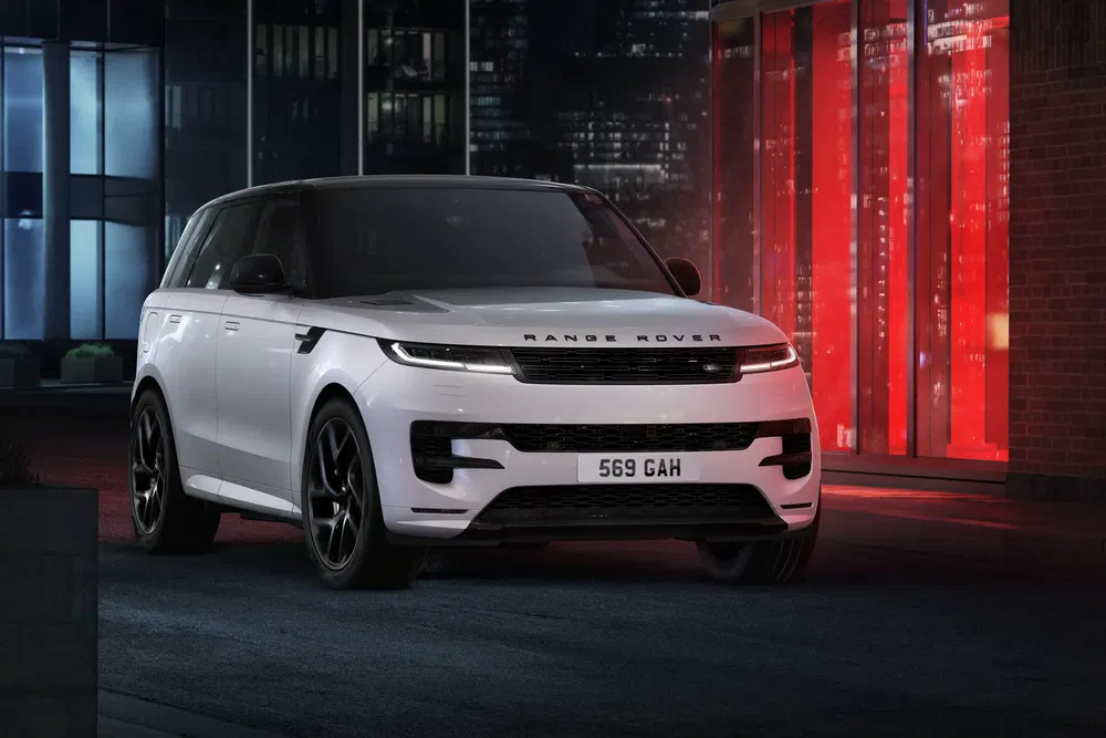 Range Rover blanc moderne, stationné devant un bâtiment urbain éclairé en rouge la nuit.