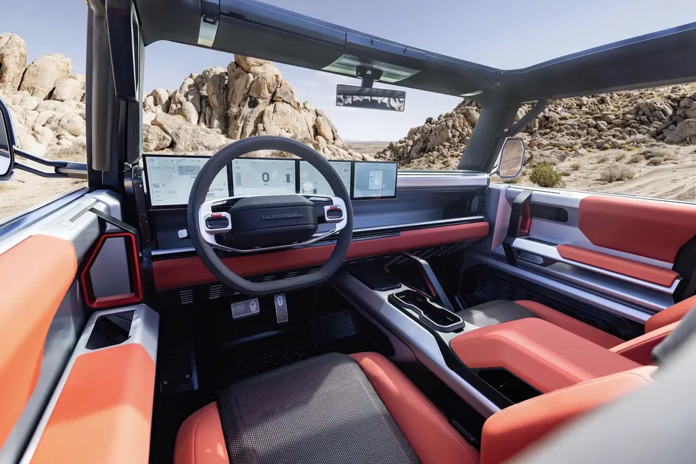 Intérieur du GMC Hummer EV, design moderne, tableau de bord numérique, sièges orange et noir.