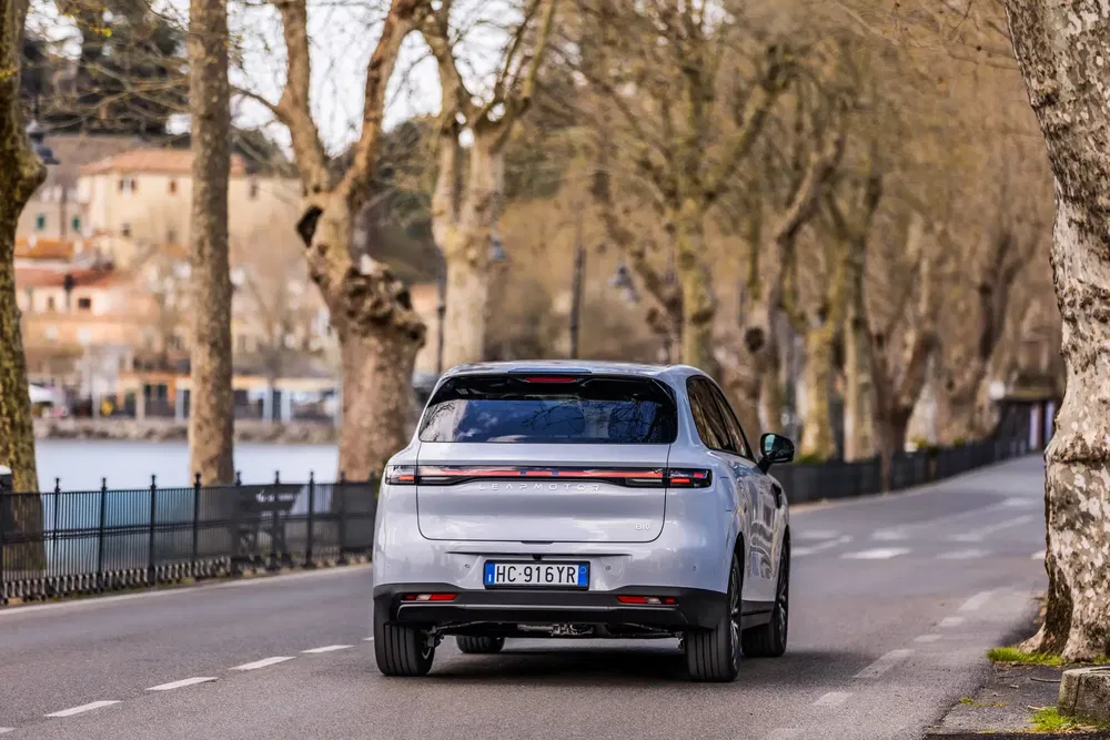 Porsche Cayenne rijdt op een boomrijke weg, Italiaanse kentekenplaat zichtbaar aan de achterkant.