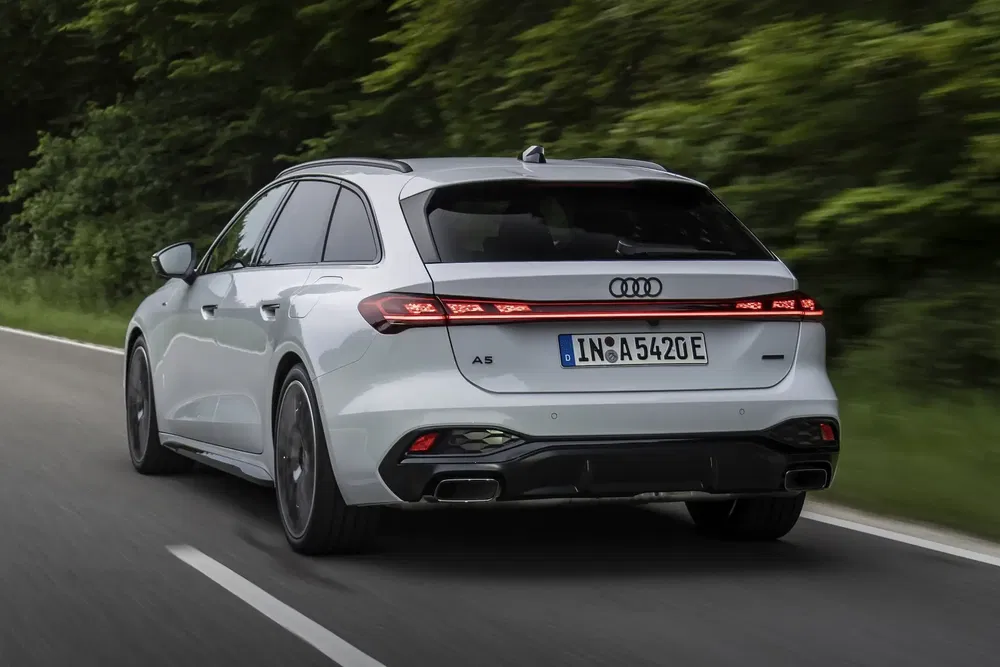 Grijze Audi A5 Sportback op een weg omgeven door bomen, dynamische achteraanzicht.