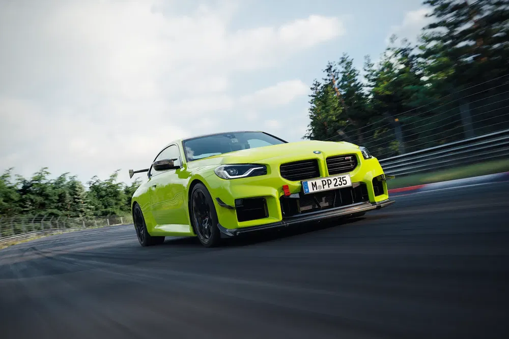{"fr":"BMW M2 2023 jaune vif en pleine vitesse sur circuit densement arboré.","nl":"Felgele BMW M2 2023 scheurt door bocht op bebost circuit."}