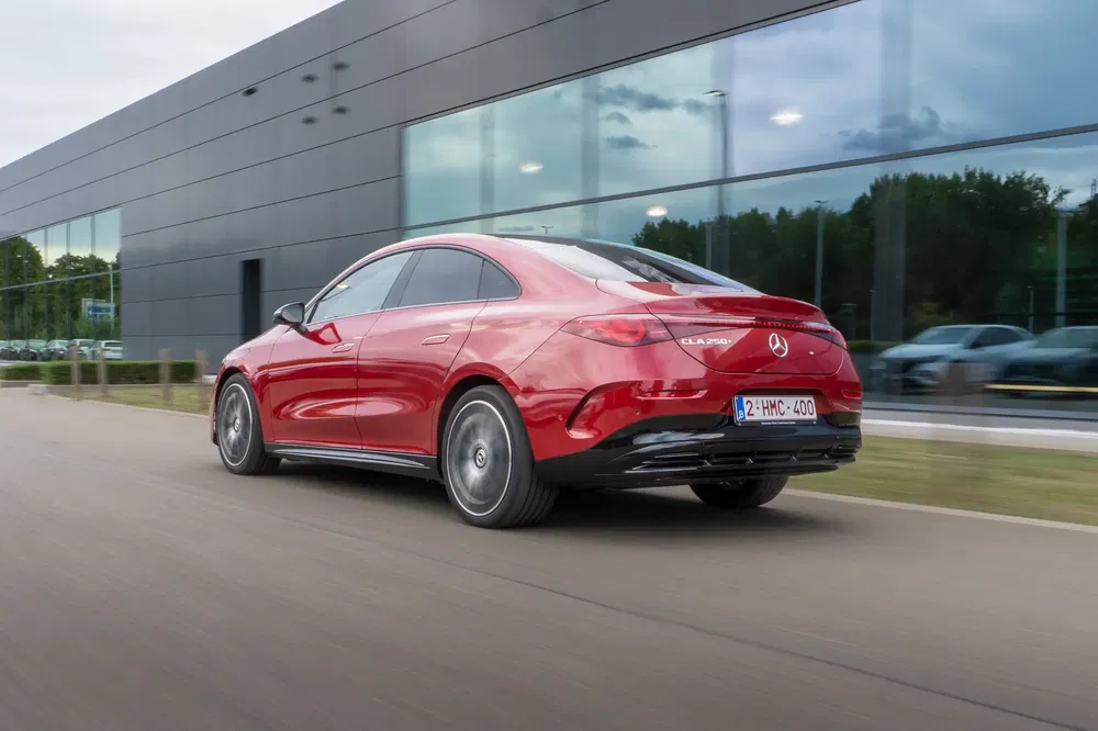 Rode Mercedes-Benz CLA 250 rijdt langs modern gebouw.