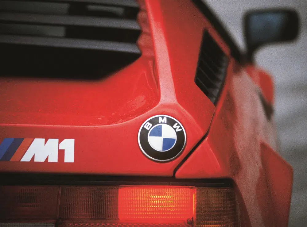 Arrière de la BMW M1 rouge avec logo BMW visible, détaillant l'emblématique supercar sportive.