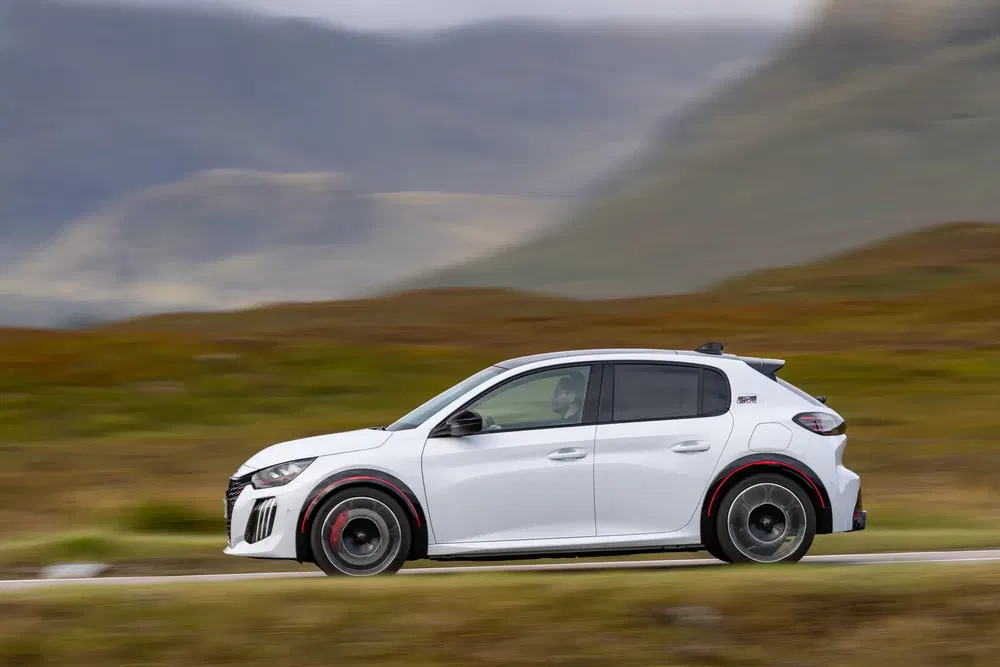 Peugeot 208 GTI blanche roulant sur route de campagne pittoresque.