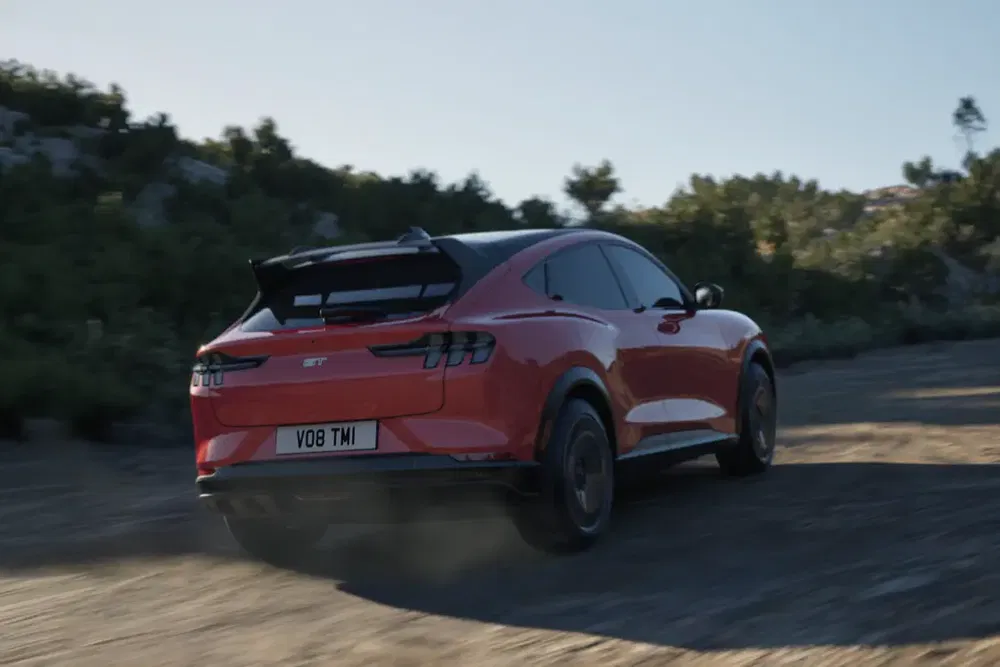 Ford Mustang Mach-E rouge roulant sur route de campagne poussiéreuse.