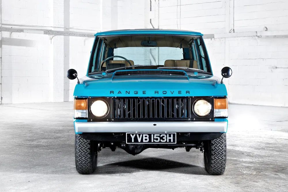 Range Rover classique bleu vif, vue de face dans un garage blanc moderne.