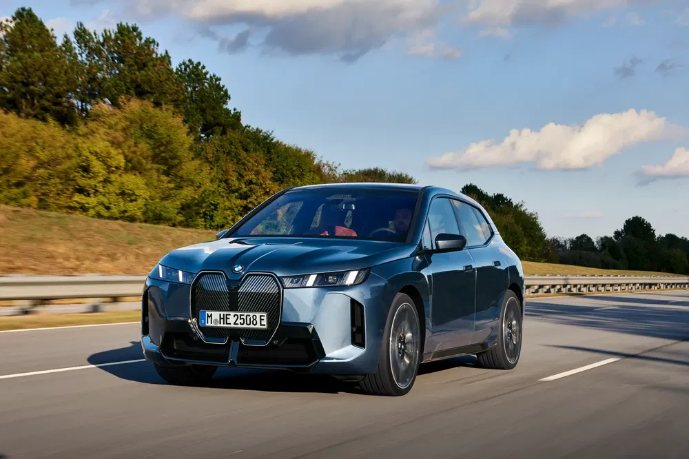 Elektrische blauwe BMW iX rijdt op snelweg met bomen op de achtergrond.