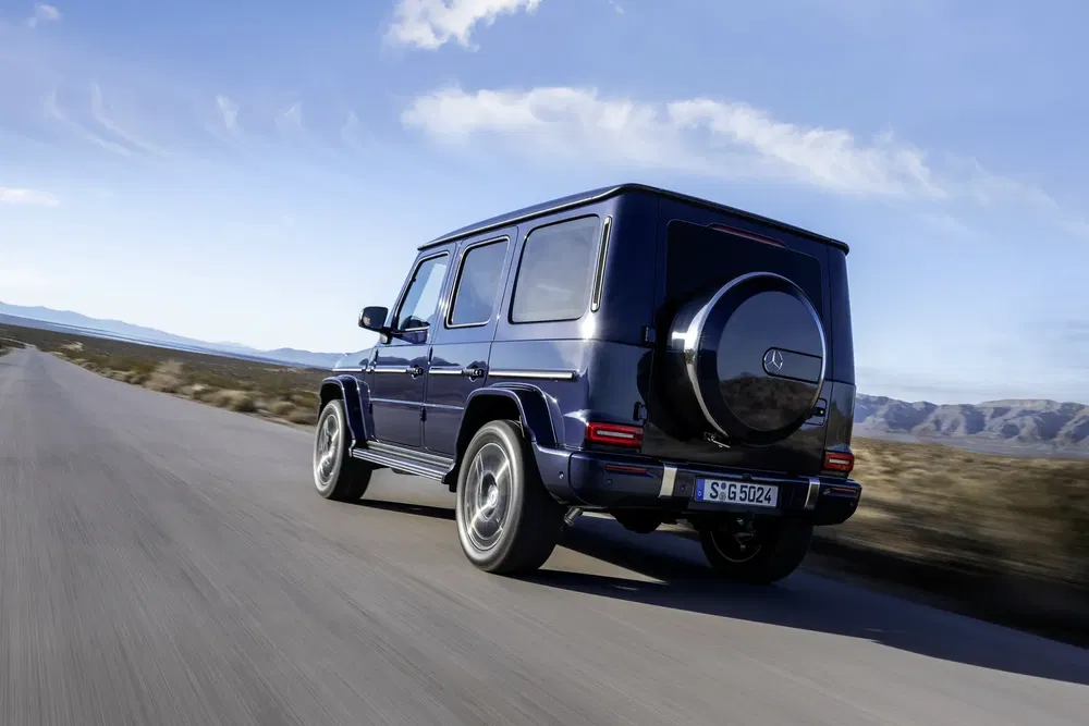 Mercedes-Benz G-Klasse rijdt op een verlaten weg onder een heldere lucht.