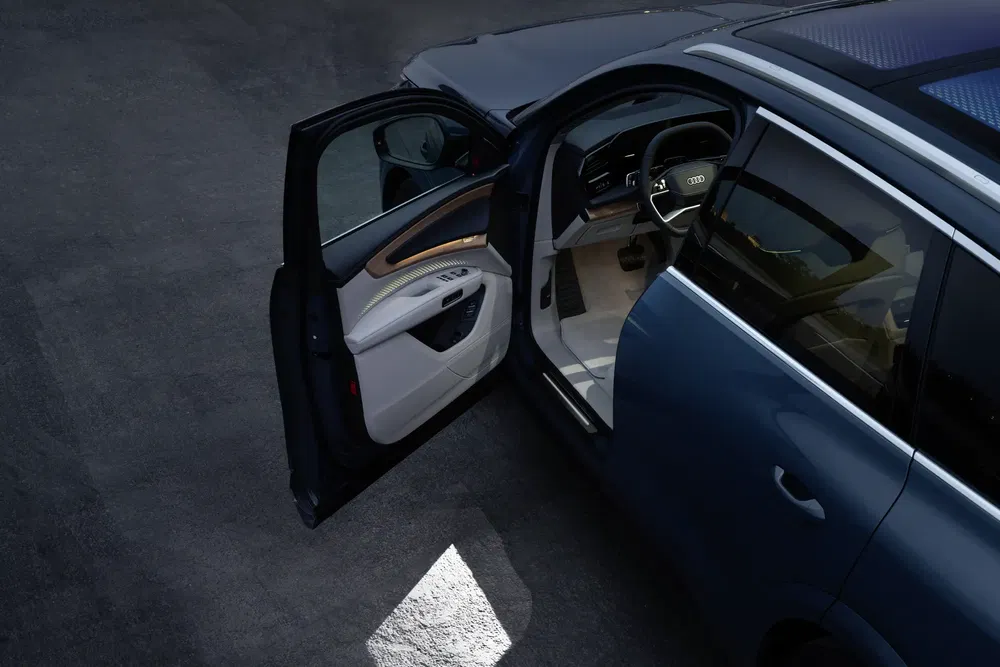 Intérieur luxueux d'une Audi avec porte avant ouverte, volant et tableau de bord visibles.