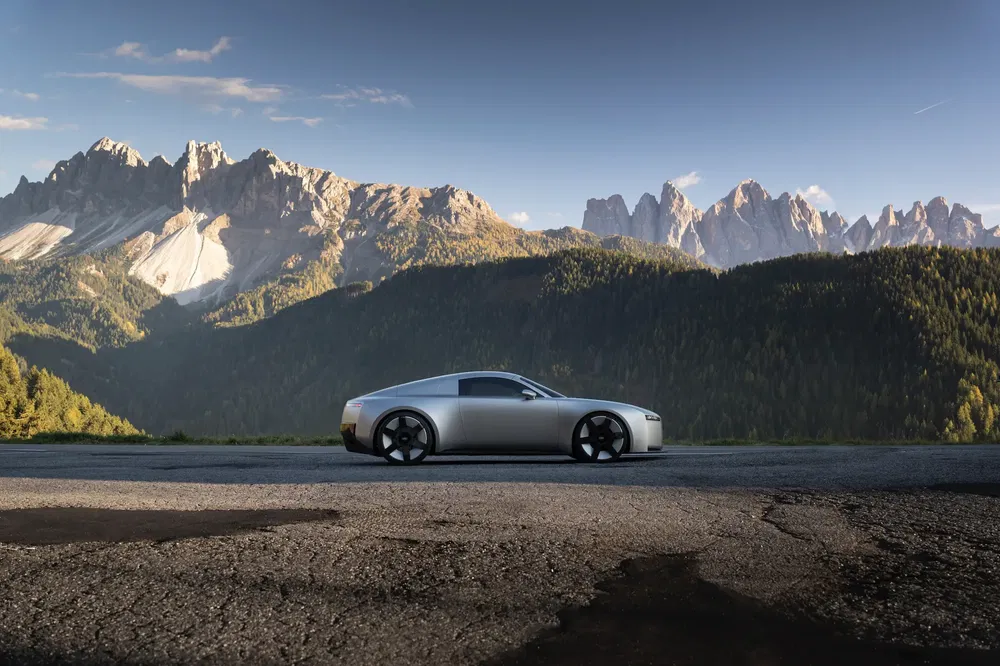 Voiture argentée élégante devant montagnes majestueuses, ciel dégagé en arrière-plan.