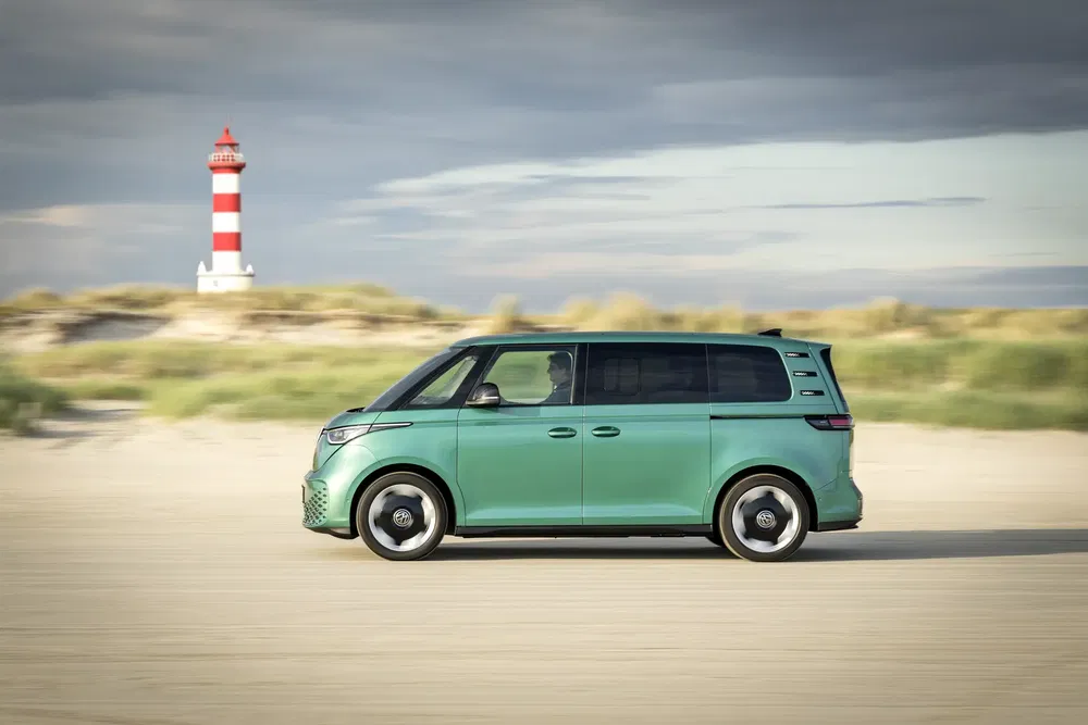 Volkswagen ID. Buzz vert sur plage avec un phare rouge-blanc en arrière-plan.