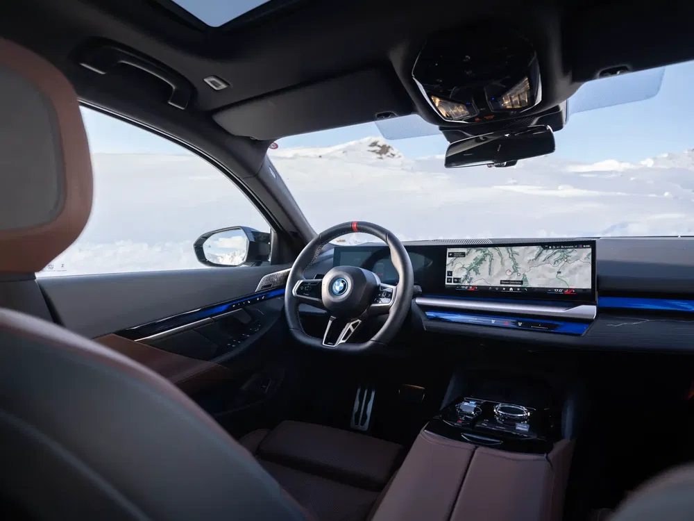 Intérieur de BMW moderne avec tableau de bord numérique, volant sportif et paysage enneigé en arrière-plan.