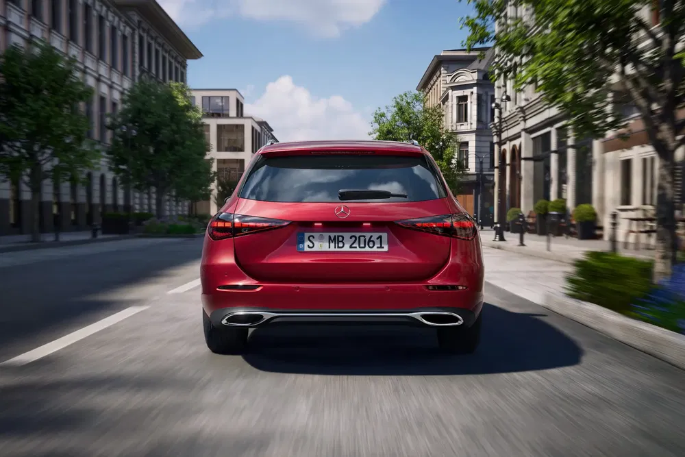 Vue arrière d'une Mercedes-Benz rouge circulant en ville sur une route bordée d'arbres.
