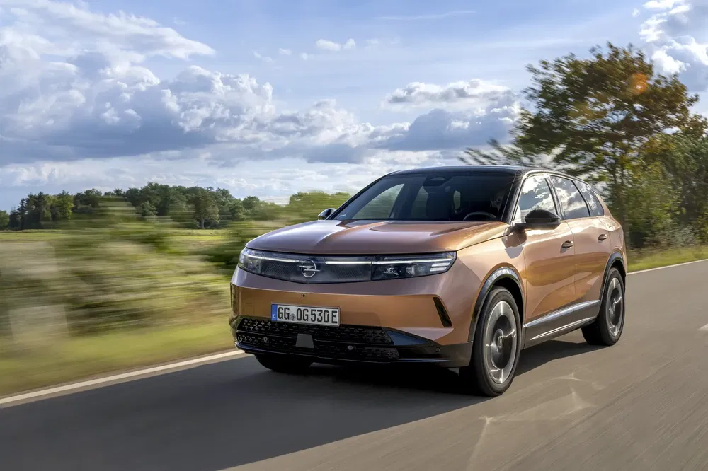 Opel SUV électrique roulant sur une route de campagne sous un ciel partiellement nuageux.
